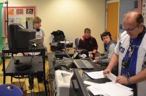Instructor David Haviland (right) reviews final scripts for the broadcast show as students work behind the scene to ensure a quality production.