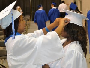 Preparations for graduation take place in the auxiliary gym as Ebonee Allen (left) centers the cap of Faythe Haskell (right).