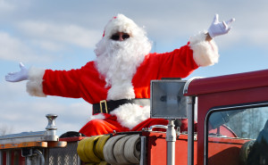 Santa Claus embraces the cheers from children as he sits atop a fire truck.