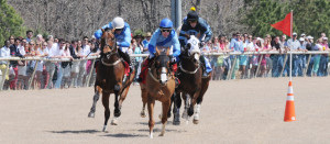 Horses and riders gallop around the final turn and into the home stretch as spectators look on.