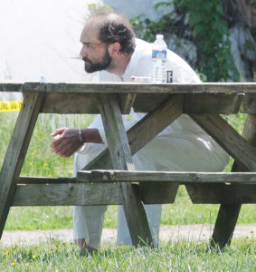 One suspect, identified by authorities as Nathaniel Atkins, 23, sits with his hands shackled at a picnic table outside the trailer that was raided by the SWAT team. He is wearing a white jumpsuit after going through a decontamination process. He has been charged with one count of heroin possession.